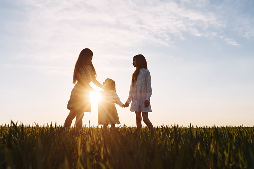 Mother with her two daughters standing in the sunrise on the field at summer.