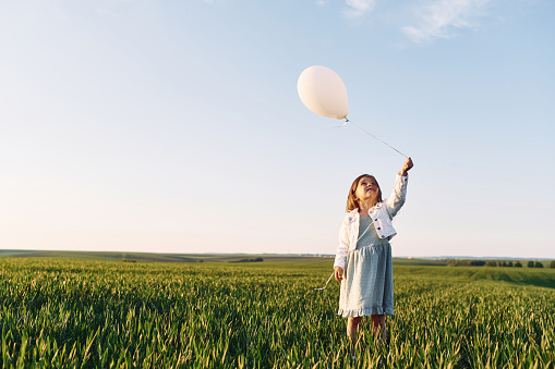 Holding balloon. Happy girl have a walk outdoors on the field at summer.