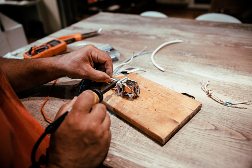 Engineer male hands Repairing and recycling old or broken electrics in his workshop. Close up on man hands using soldering iron wire to fix broken electronics
