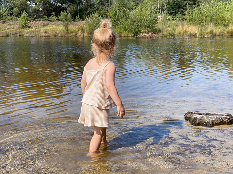 Toddler girl playing near the water of the Roode Beek river in the Brunssummerheide Heath land on a warm summer day in August.