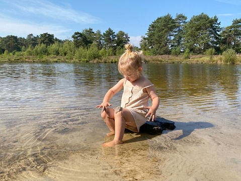 Toddler girl playing in the water of the Roode Beek river in the Brunssummerheide Heath land on a warm summer day in August.