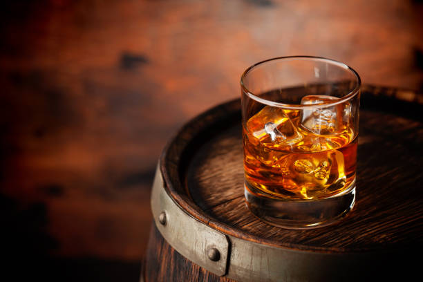 Glass of whiskey with ice cubes on the old barrel Glass of whiskey with ice cubes on the old barrel. With copy space on wooden background rum stock pictures, royalty-free photos & images