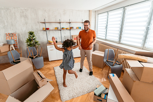 Caucasian young man dancing with his multiracial child in their new apartment.