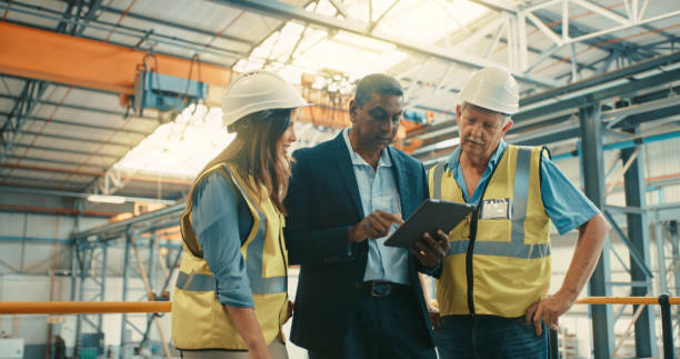 chef d’équipe montrant des conceptions sur tablette numérique et instruisant les travailleurs de la construction d’entrepôt sur un projet. des employés sérieux qui écoutent leur superviseur, leur gestionnaire ou leur patron leur dire des plans de - engineer occupation women industrial photos et images de collection