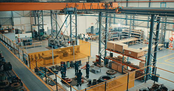 Overhead of a construction factory, warehouse or industrial plant with a team working on maintenance, repair or production. Engineering, manual labor and blue collar work in a commercial workshop