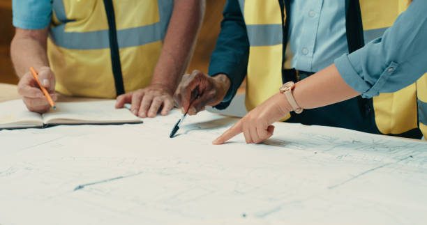 istock Closeup of creative group of architect design engineers working on blueprint construction building plans together. Team of professional home designers discussing architecture project 1415590761