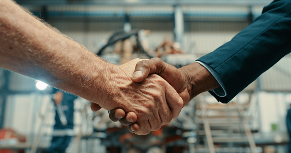 A professional handshake after a successful b2b collaboration meeting in a factory warehouse. Men shaking hands in compliance and sealing a business contract deal for a trustworthy insurance company