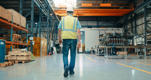 istock Manufacturing manager, logistics supervisor or engineer walking inside warehouse, factory or workshop with industry background and copy space. Behind of mechanic or electrician in industrial building 1415590788