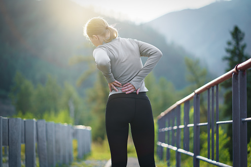 Back view of adult runner woman suffering from Backache or Sore waist after running.