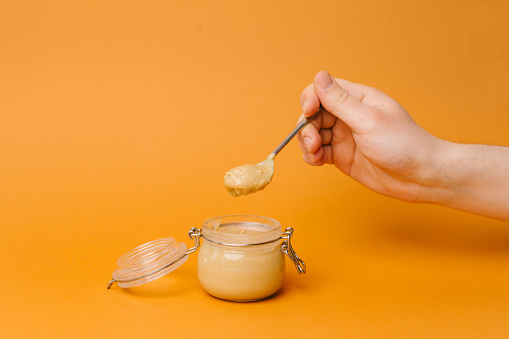 A small jar with peanut butter on a plain yellow background