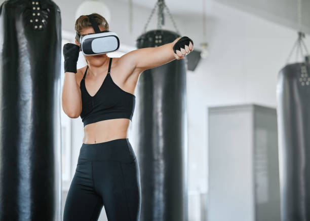 istock Healthy, fit and active boxing woman with a VR headset to access the metaverse while exercising, training and working out in a gym. Female boxer doing a workout in virtual reality with technology 1415594198