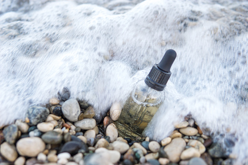 Cosmetic serum for the skin in a glass bottle. A bottle with an eyedropper on a pebble beach by the sea. Essences for skin care on the background of stones. The concept of natural cosmetics and SPA products.