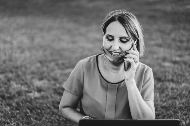 istock Woman 40 years old working outdoors with laptop during coronavirus outbreak - Smiling entrepreneur sitting on lawn with personal computer while calling with cellphone - Remote work concept into nature 1415596561