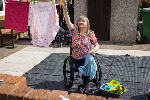 A medium wide angle of a woman who is living with cancer and is also a wheelchair user making the most of the dry weather and having her washing up outside to dry.