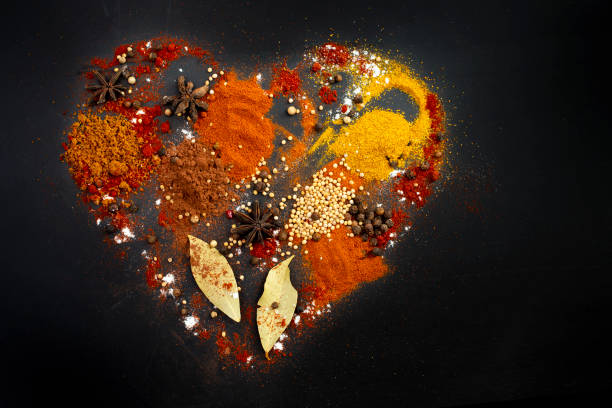 Multiple various spices forming a heart shape, isolated on black background.