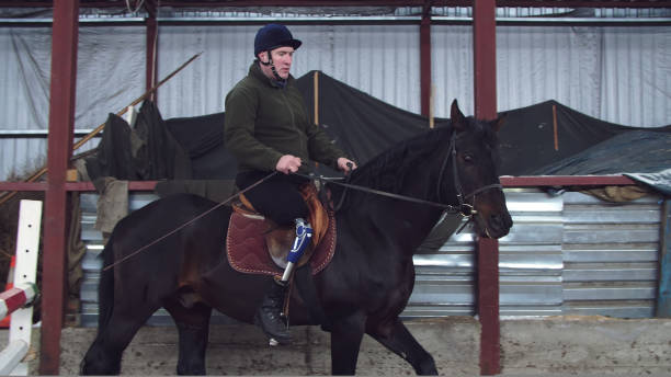 istock in special hangar, a young disabled man learns to ride a black, thoroughbred horse, hippotherapy. man has an artificial limb instead of his right leg. 1415599530