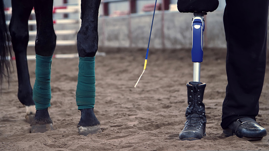 close-up, horse legs, rewound with bandage and male legs of a disabled rider. man has a prosthesis instead of his right leg. concept of sincere friendship of man and animal. Hippotherapy