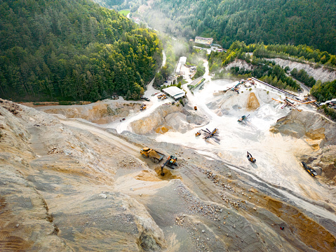 Aerial view from above of open cast mining quarry with machinery at work