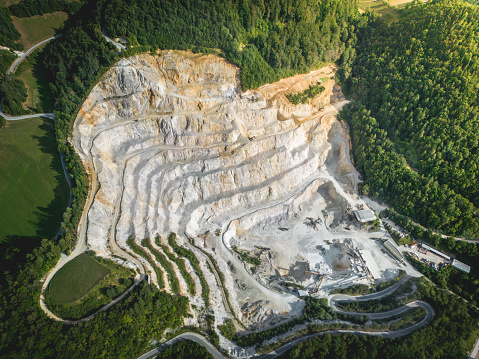 Aerial view of a mining quarry with heavy machinery, surrounded by forest at sunset.