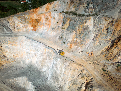 Aerial view of a mining quarry with heavy machinery, surrounded by forest at sunset.