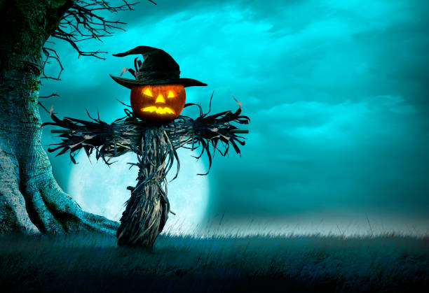 A scarecrow topped with an illuminated jack o'lantern stands in the middle of an open field framed by the trunk of a gnarled bare tree in front of a rising moon on Halloween night.