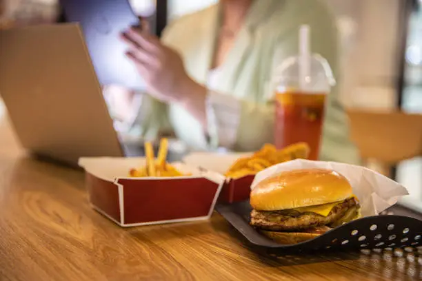 Photo of Businesswoman working at laptop with fast food on restaurant table