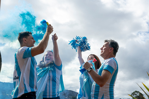 fans of the Argentinian soccer team celebrate the victory of their soccer team outdoors with blue smoke flares, flags and lots of euphoria