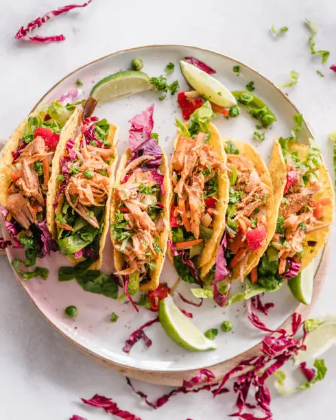Pulled jackfruit tacos served on a plate with lime wedges and fresh herbs