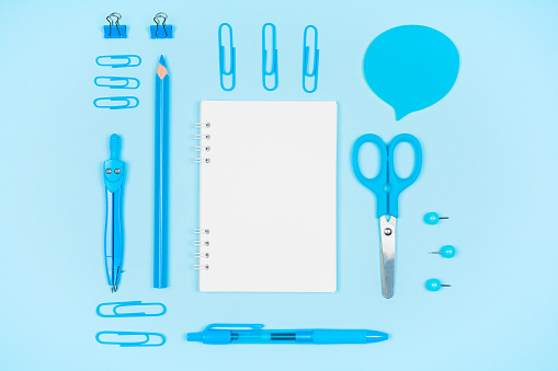 Blue school supplies and blank notepad on blue background. Top view with copy space
