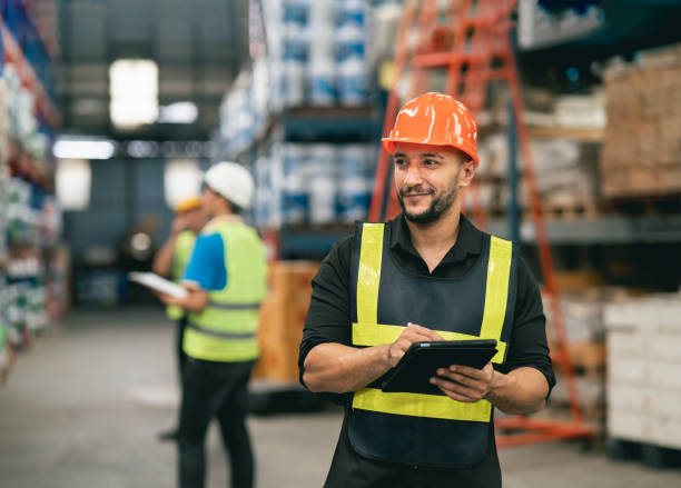 istock Professional manager man employee using tablet check stock working at warehouse. Worker wearing high visibility clothing and a hard hat, helmet and checking and count up goods or boxes for delivery. 1415613270