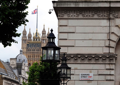 London, UK - June 24, 2022: Downing Street sign on the wall of a building in London with the Houses of Parliament in the background.