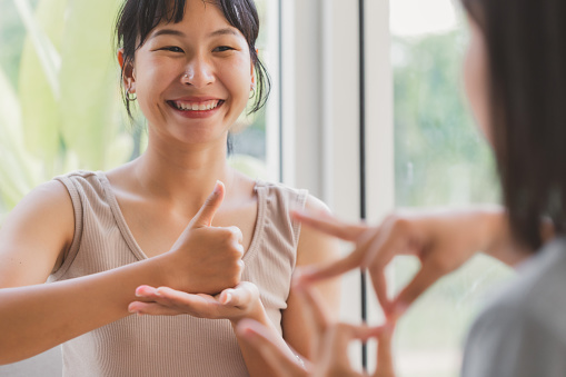 Mujeres asiáticas jóvenes y atractivas que usan la conversación en lenguaje de señas con los dedos de la mano con personas sordas. Alegre feliz utilizando la comunicación no verbal a personas con discapacidad. photo
