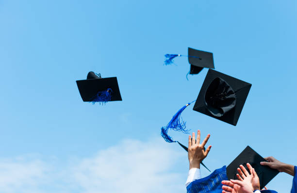 istock Graduating students hands throwing graduation caps in the air 1415614817