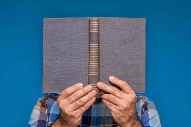 istock Close up man hand holding a book to read. reading concept, reader hiding behind a book, book head. Learning, studying. 1415616646