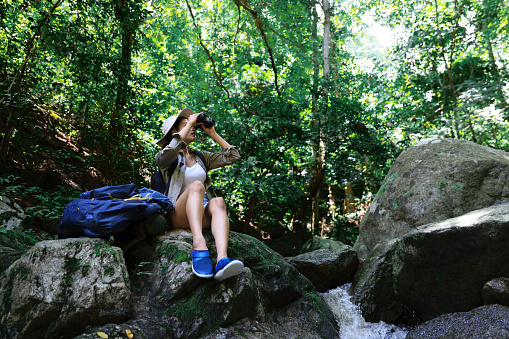 Young female back pack trekking travel in forest, beautiful tourist site to rest on rock at waterfall river in forest ,  adventure travel lifestyle