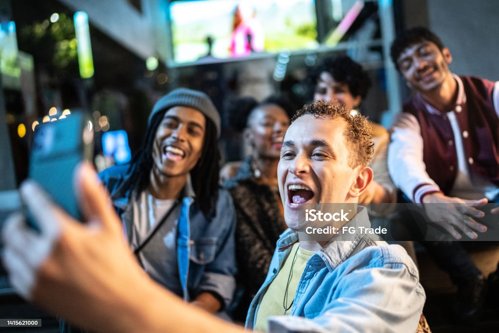 Man filming (or taking selfie/video call) using mobile phone with friends enjoying nightlife Youth Culture Stock Photo