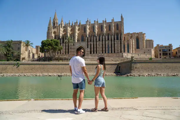 Photo of Couple in love gazing into each other's eyes with sunglasses and the famous cathedral of Palma de Mallorca in the background.