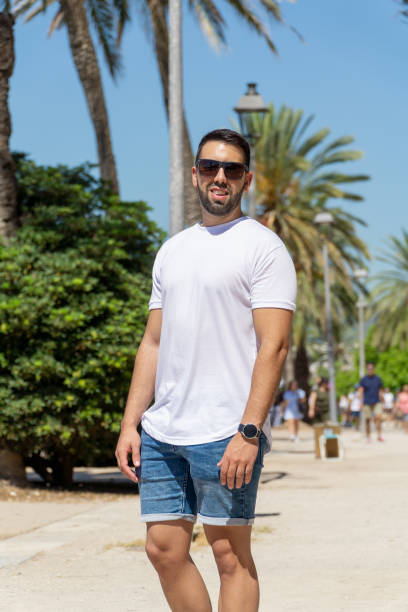 istock Young man with beard and sunglasses posing with palm trees in background 1415622274