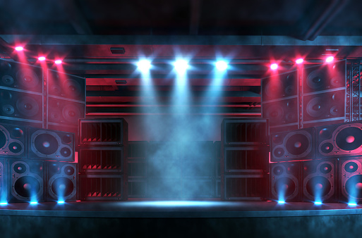Empty music concert stage illuminated by bright spotlights, with smoke and flares, surrounded by a large and loud sound system with plenty of loudspeakers. Punk and rock music background with copy space for adding items and characters. Digitally generated concert backdrop.