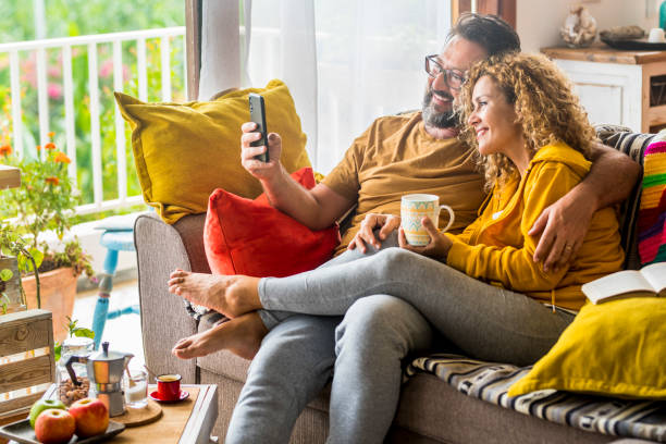 istock Smiling Couple Taking Selfie Through Smart Phone Sitting On Sofa 1415625889