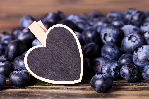 Ripe blueberries with decorative wooden heart on brown background.