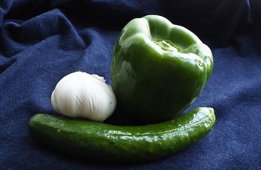 Green bell pepper ( paprika, sweet pepper, pepper or capsicum ) , Cucumber ( cucumis sativus ) and garlic on blue background