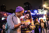 Young couple (or friends) using mobile phone at festival by the night - including a transgender person
