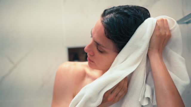 A young woman wiping her face and hair with a white towel after a shower