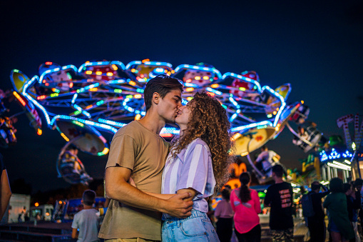 Happy young couple enjoying together at the amusement park at night