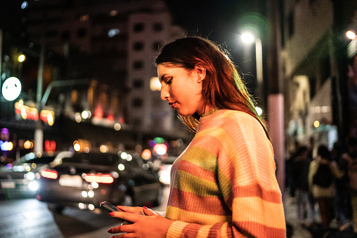 Transgender woman using the mobile phone in the street at night