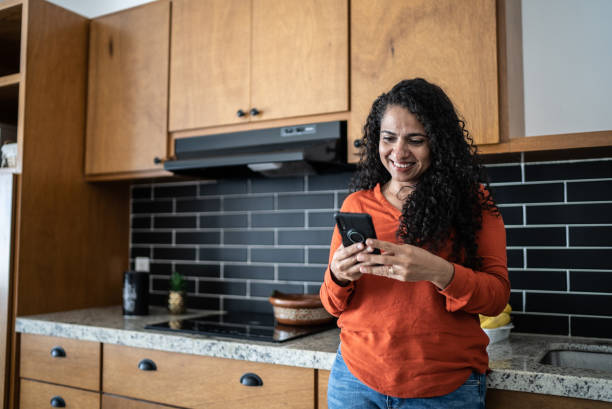 istock Mid adult woman using mobile phone in kitchen at home 1415638401