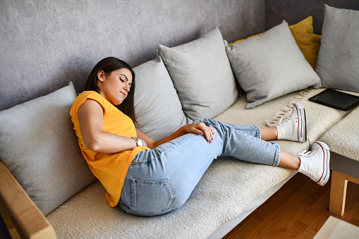 Female With Menstrual Cramps Curling Up On Sofa