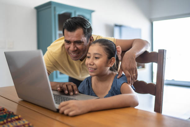 istock Father helping daughter studying on the laptop at home 1415641417