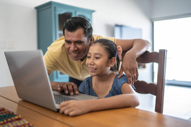 Father helping daughter studying on the laptop at home stock photo